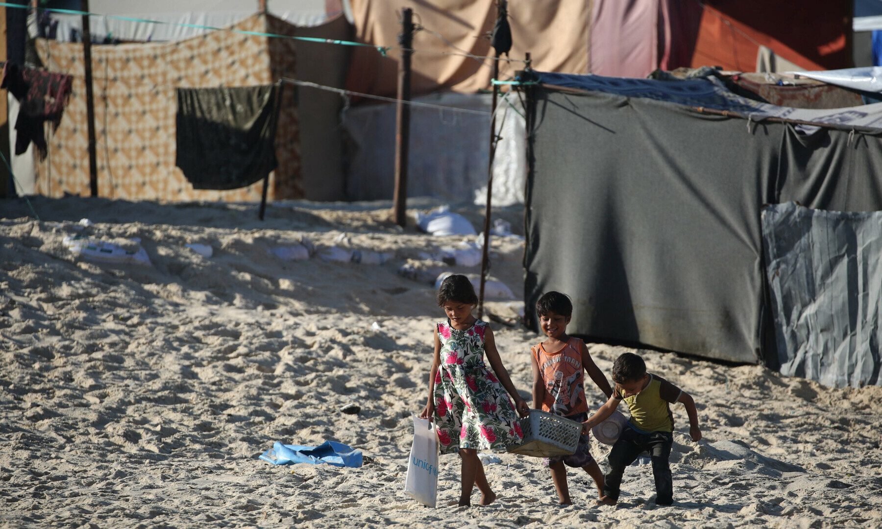  Displaced Palestinian children carry a crate back to their tent at a makeshift camp on the beach of Gaza City on Oct 13, 2024. &mdash; AFP 