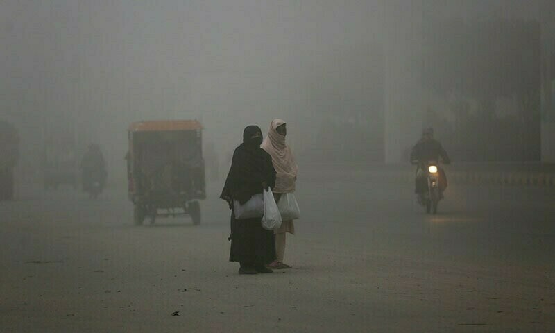 Women wait for transportation as heavy fog reduces visibility, in Lahore. &mdash; AP