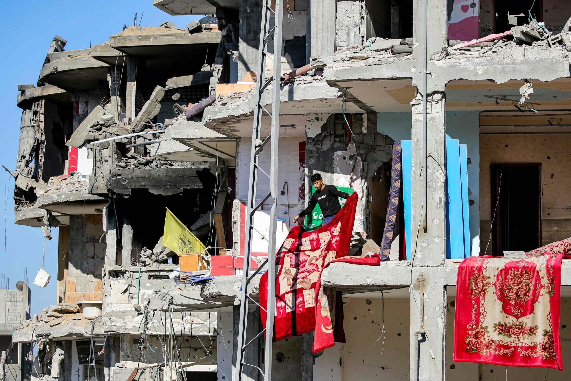 A youth lays out blankets to air in the sun in a heavily-damaged building with no remaining front walls in Rafah in the southern Gaza Strip on January 21. &mdash; AFP