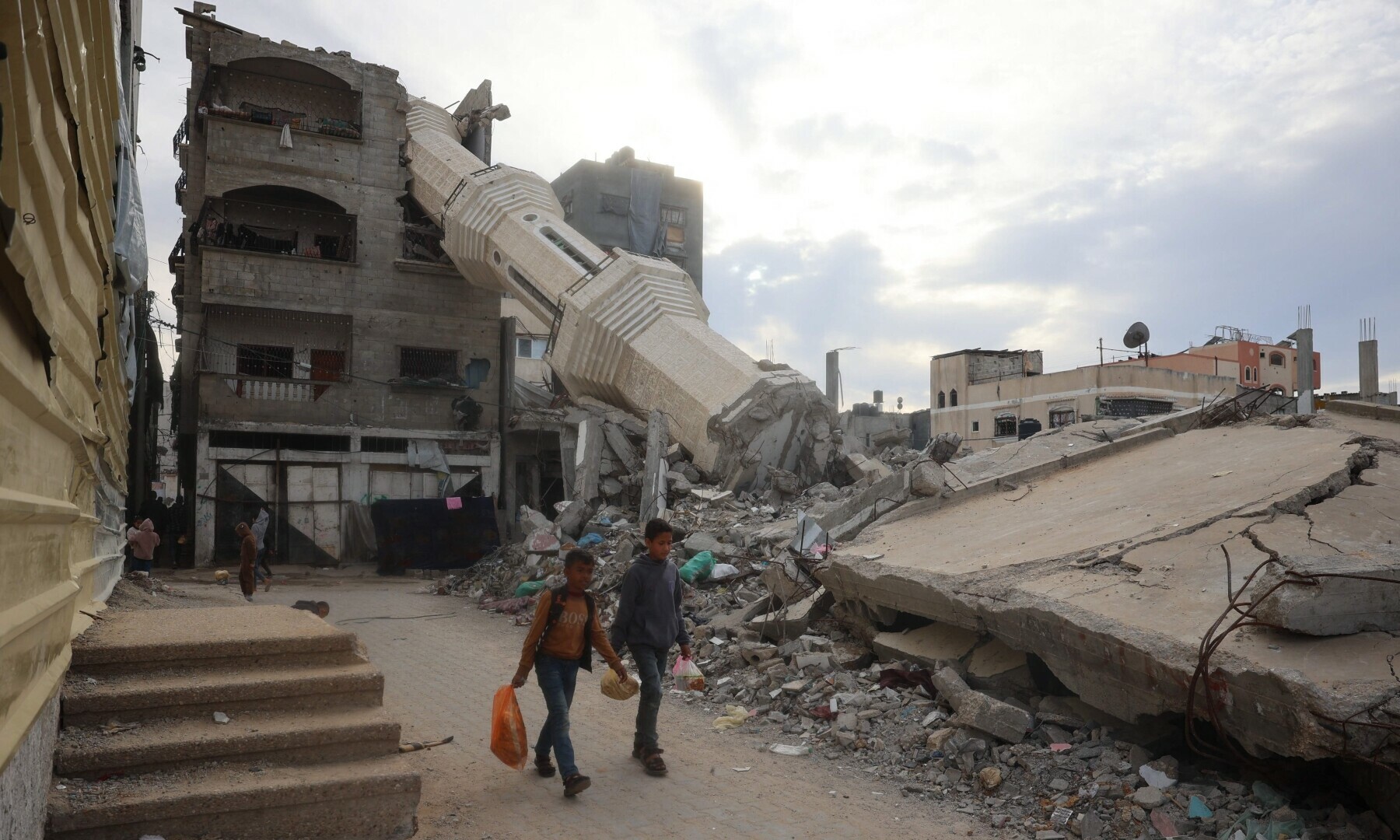 Palestinian children carry food past destroyed buildings at the Nuseirat refugee camp in the central Gaza Strip on March 3, 2025 during Ramazan. — AFP