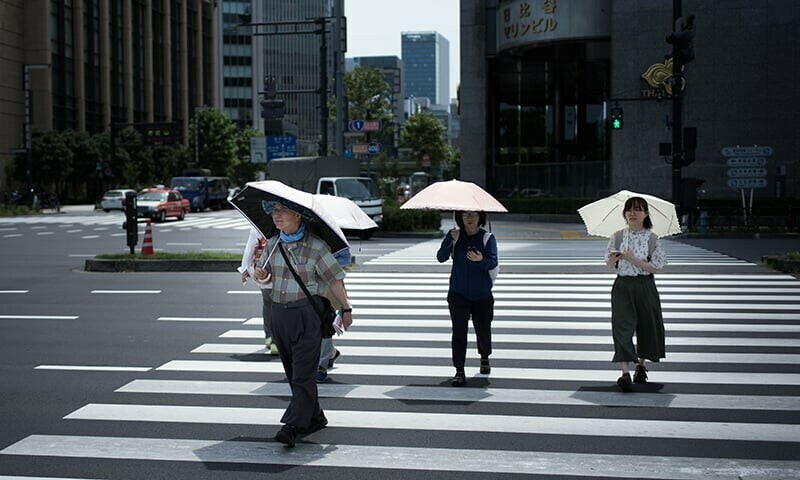 People hold umbrellas as they walk along a street in Tokyo. — AFP/File People hold umbrellas as they walk along a street in Tokyo. — AFP/File