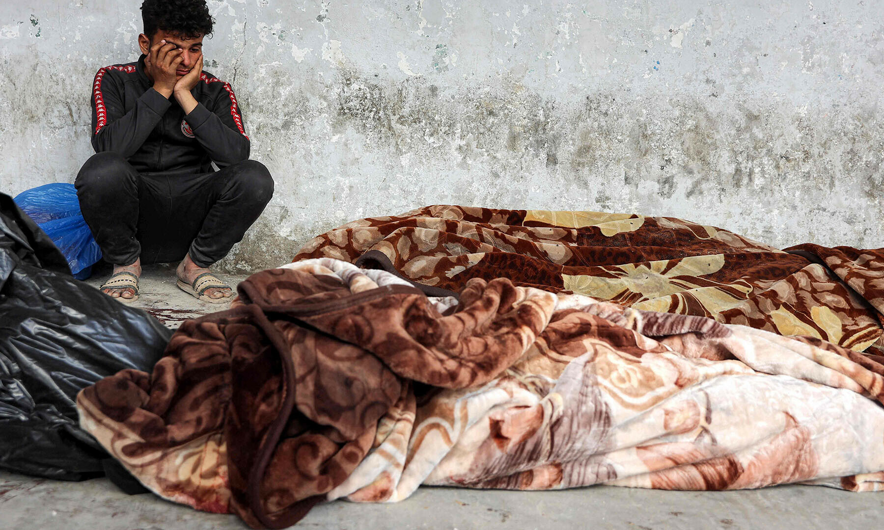 A boy reacts as he sits next to the bodies of victims who were killed in Israeli bombardment in Gaza City, as they lie wrapped in blankets at the Ahli Arab hospital in Gaza City on March 18. — AFP