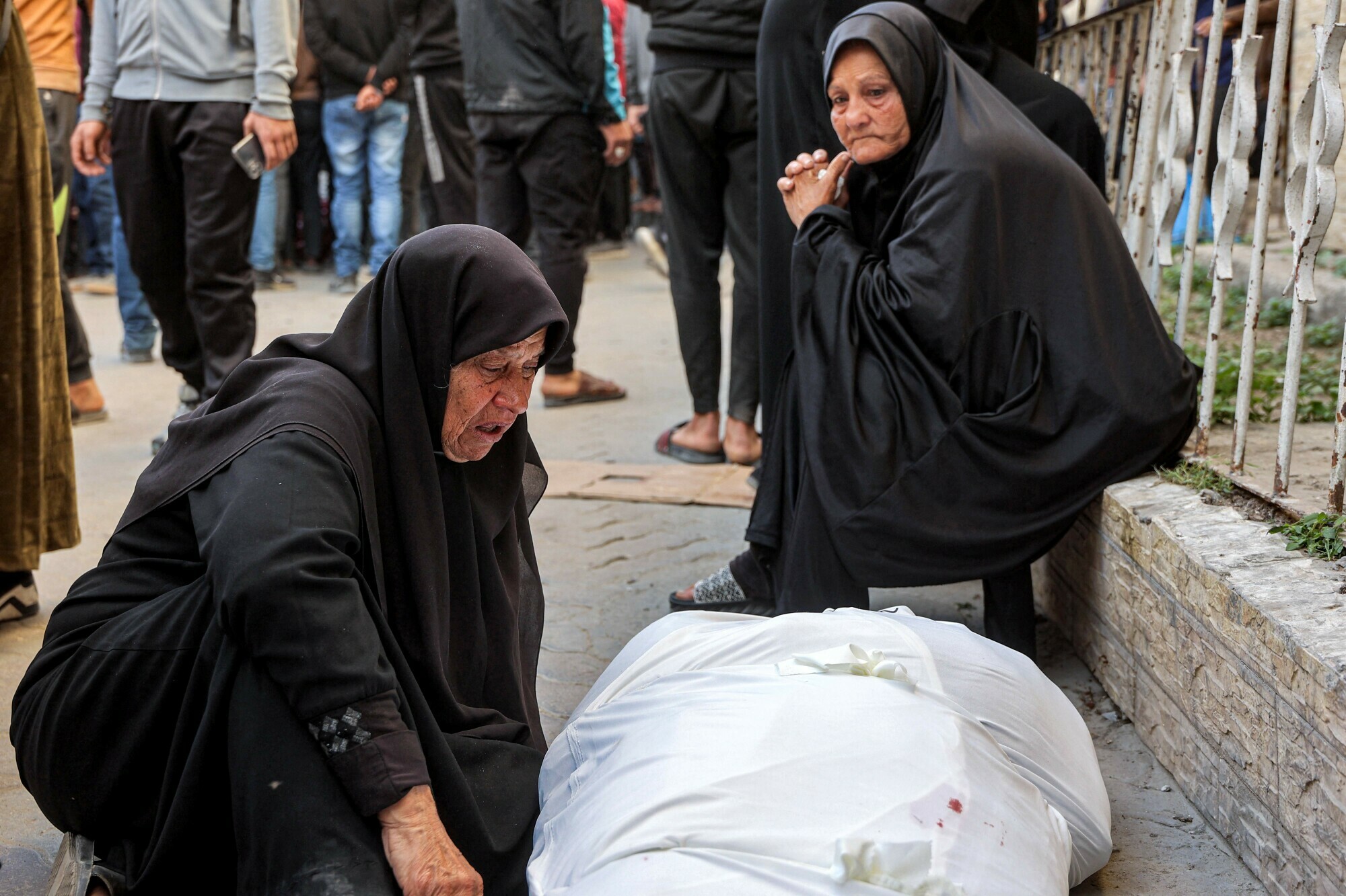 An elderly woman reacts as she sits in mourning next to the shrouded body of one the victims killed in Israeli bombardment, at the Ahli Arab hospital in Gaza City on March 18. — AFP