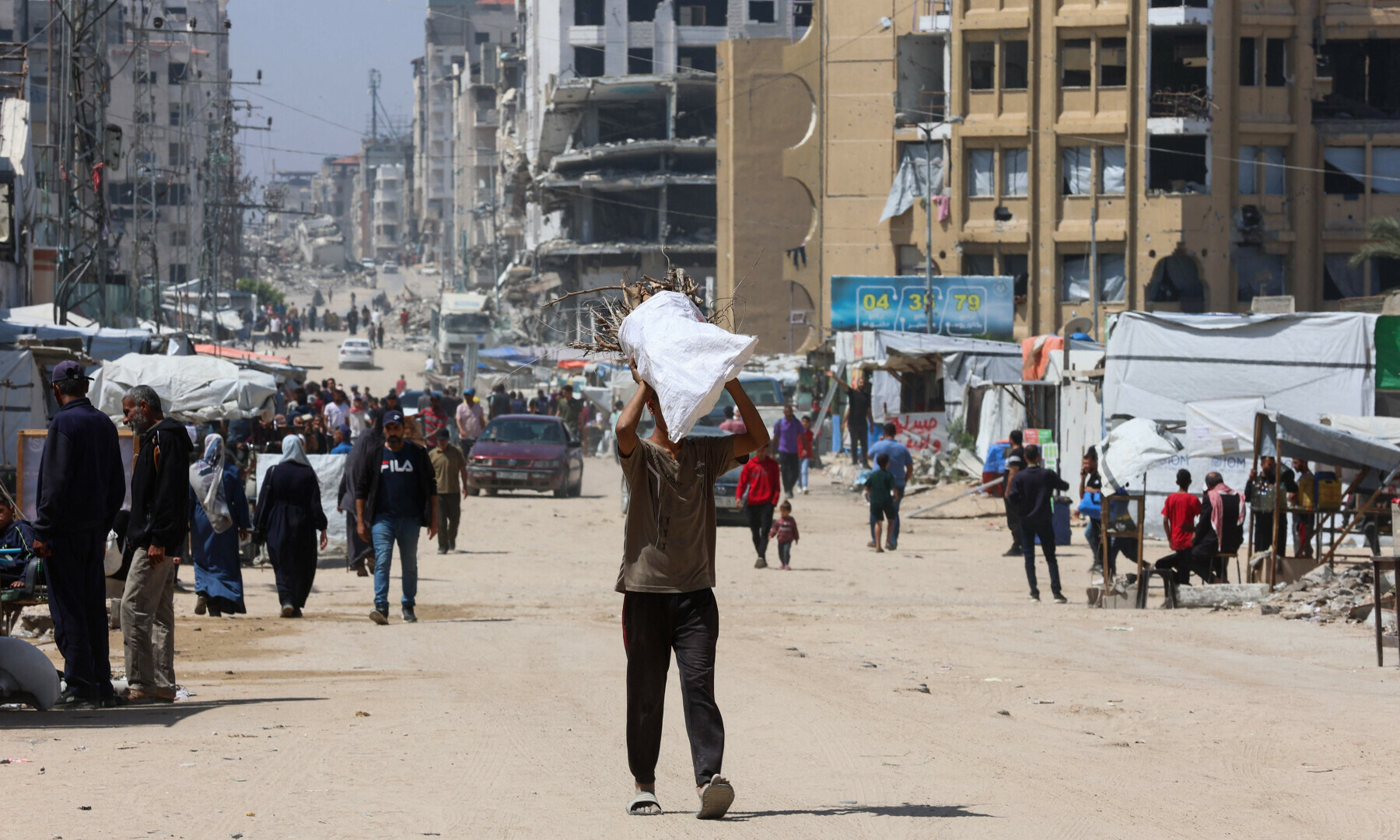 A Palestinian man carries collected wood as he walks past makeshift displacement tents in Gaza City on May 1, 2025. — AFP