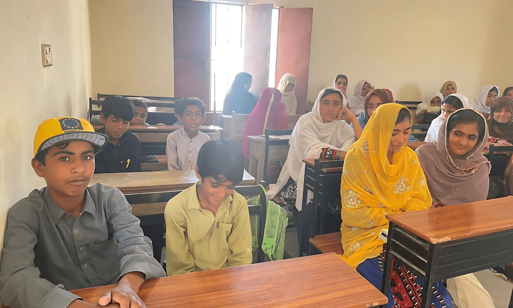 Usman and his mates sit on benches inside the classroom.