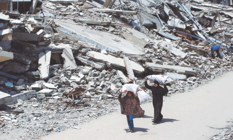 A Palestinian woman and a girl, carrying bags of firewood, walk by the rubble of houses in Gaza City 
on Tuesday.—Reuters