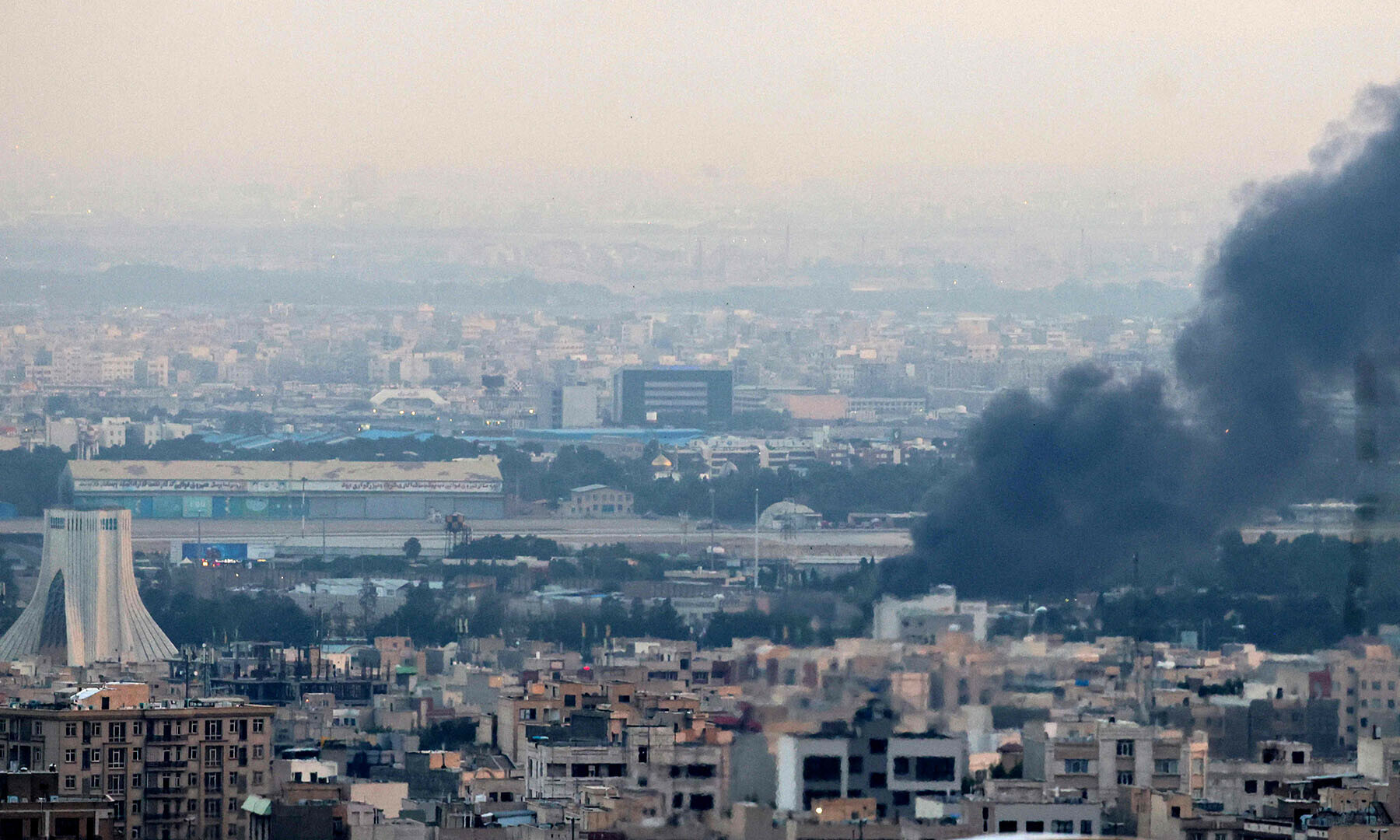Smoke billows from a site near the Azadi Tower (L) in central Tehran, as fighting between Israel and Iran continues on June 16, 2025. Israel and Iran traded deadly fire on June 16 in their most intense confrontation in history, fuelling fears of a drawn-out conflict that could engulf the Middle East. (Photo by ATTA KENARE / AFP)