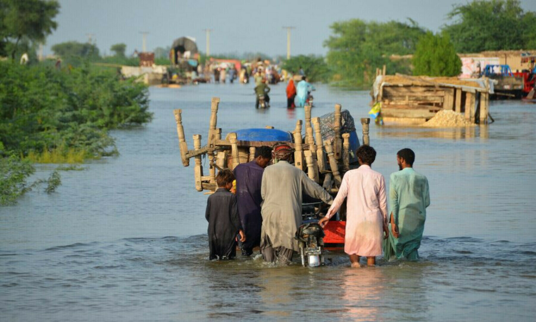Men walk along a flooded road with their belongings, following rains and floods during the monsoon season in Sohbatpur, Pakistan on August 28, 2022. — Reuters/Amer Hussain