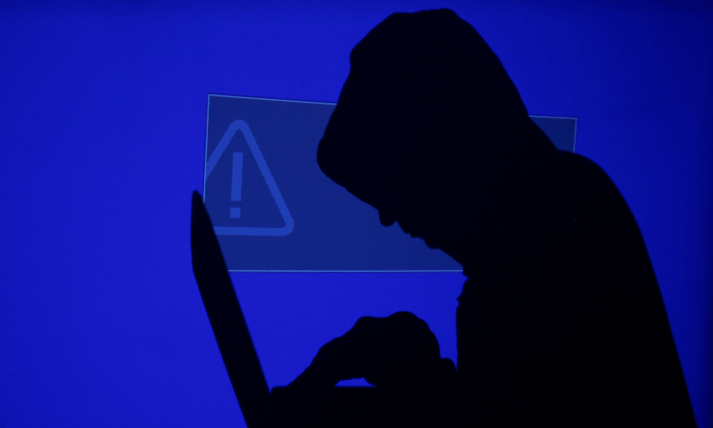 A hooded man holds a laptop computer as blue screen with an exclamation mark is projected on him in this illustration picture taken on May 13, 2017. —Reuters