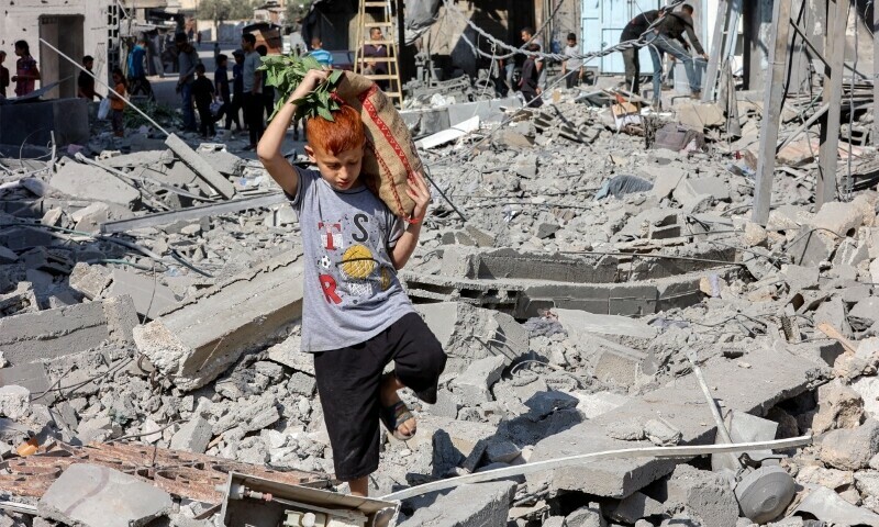 A boy walks with a sack on his back through rubble along a street following Israeli strikes in Jabalia in the northern Gaza Strip on June 27. &mdash; AFP