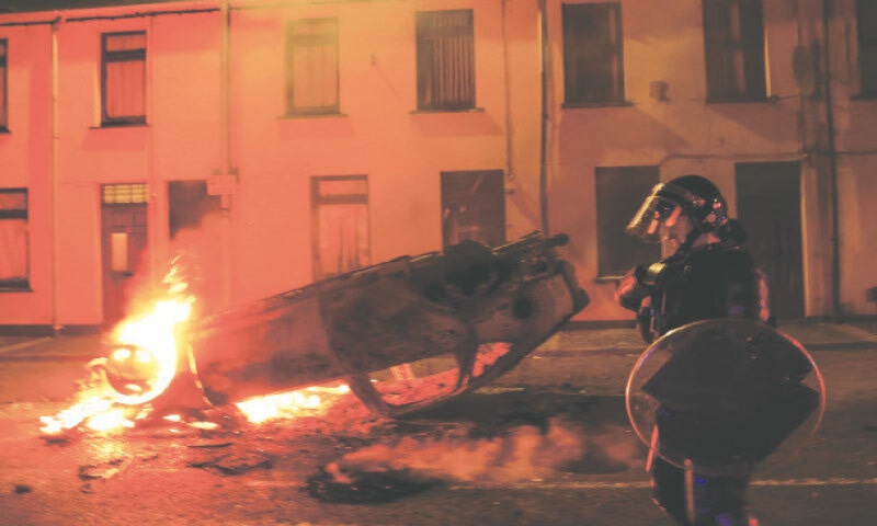 Ballymena: A police officer operates near a burning vehicle during a second night of riots on Wednesday.—Reuters