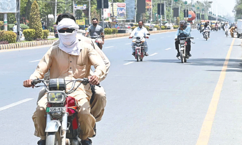 SARGODHA: A motorcyclist covers his face and head with cloth amid an intense heatwave.—APP
