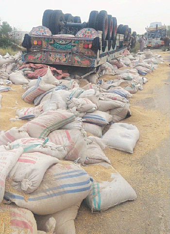 The overturned trailer lies on the road with wheat sacks scattered around it. — Dawn