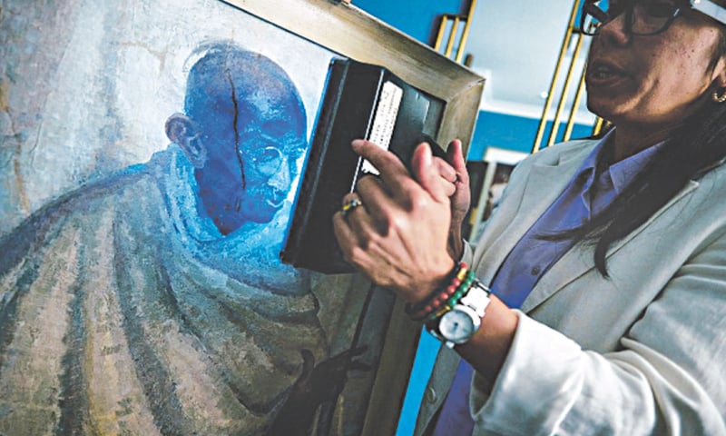 Rhyanon Demery, Bonhams Head of Sale for Travel and Exploration, uses UV light to show the spot where the now-restored painting by British-American artist Clare Leighton of Indian independence leader Mahatma Gandhi, was once damaged at Bonhams auction house in London.—AFP