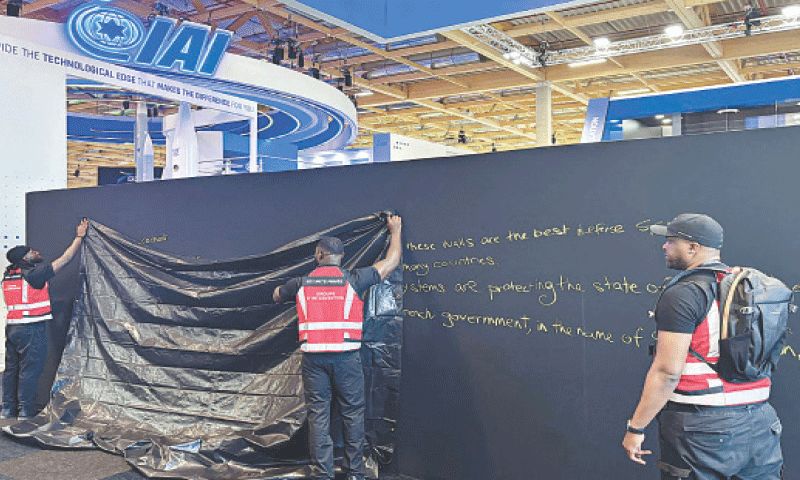 Security personnel hide a graffiti on a panel of the Israeli pavilion at the Paris Air Show. The graffiti reads ‘Behind these walls are the best defence systems used by many countries. These systems are protecting the state of Israel these days. The French government, in the name of discrimination, is trying to hide them from you!’—AFP