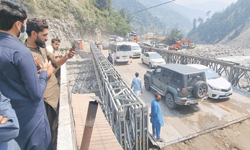 People look on as traffic flows on the newly-installed steel bridge in Mahandri area of Kaghan valley, Mansehra, on Thursday. — Photo by Nisar Ahmed Khan