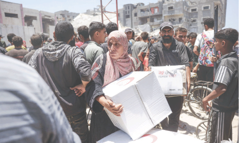 GAZA CITY: A Palestinian woman moves through a crowd of aid-seekers as people gather to receive food parcels from a distribution point supervised by volunteers.&mdash;AFP