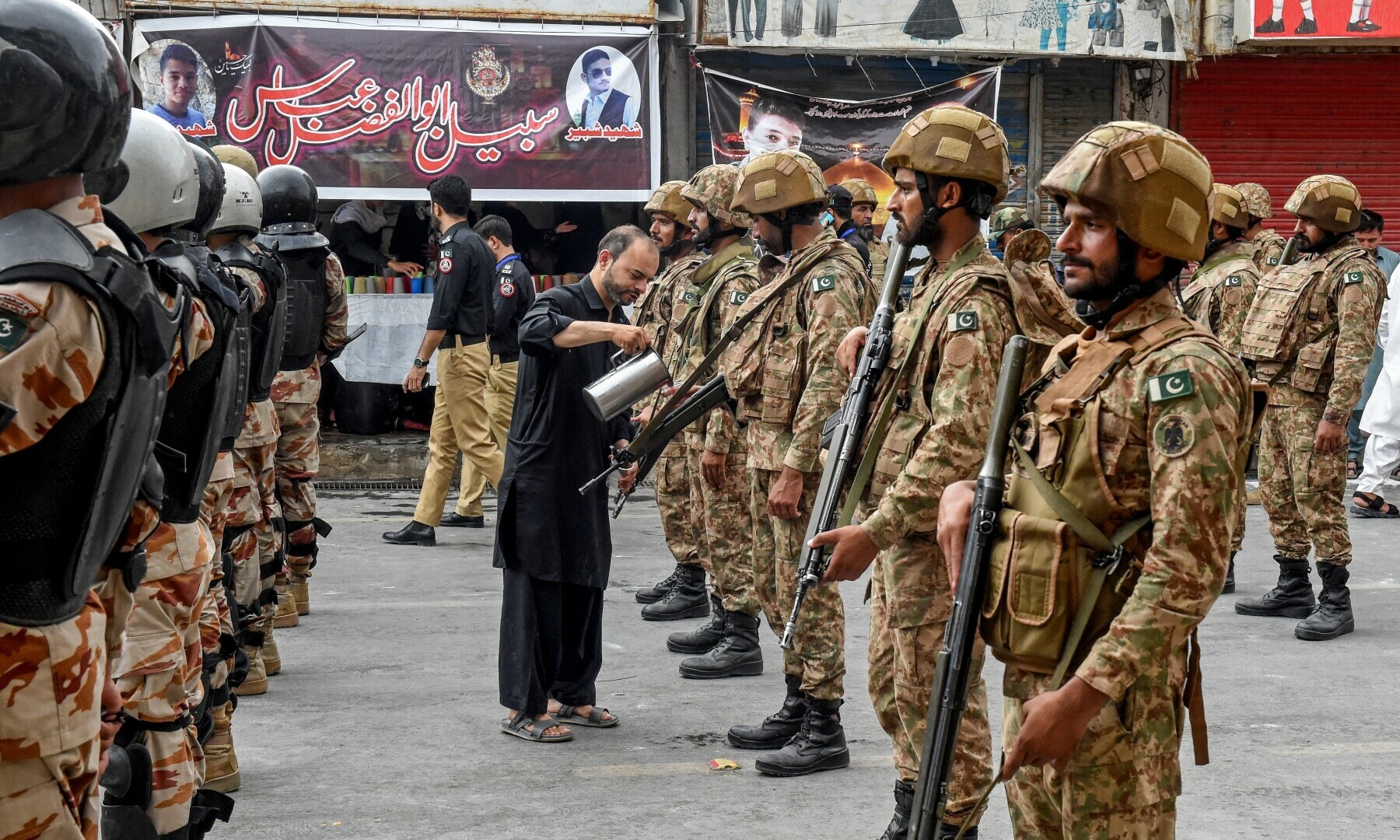 A volunteer offers drink as Pakistani soldiers escort a religious procession in Quetta, July 3. — AFP
