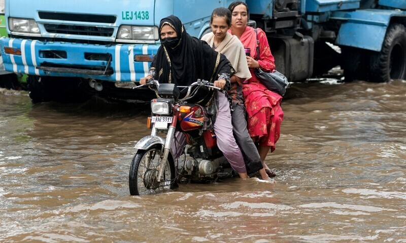 Commuters wade through a flooded street after heavy monsoon rains in Lahore on July 9. — AFP