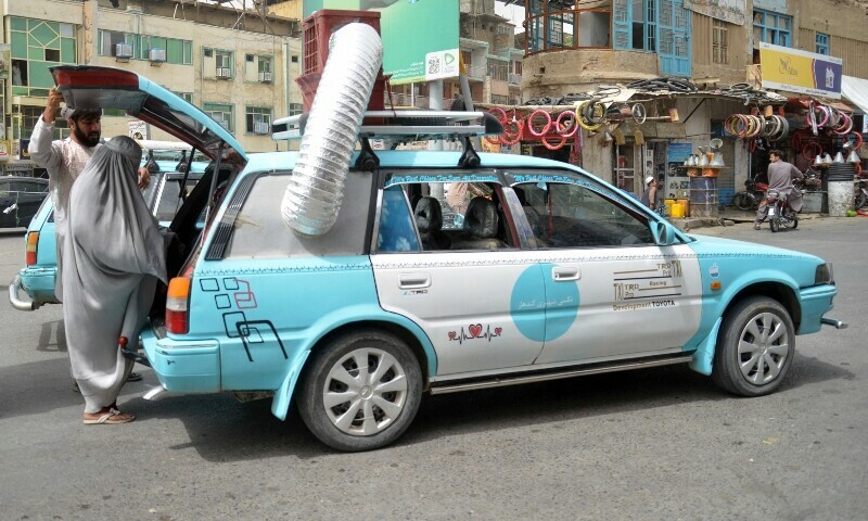 An Afghan woman boards a taxi with a swamp air-cooler system installed overhead in Kandahar, Afghanistan, July 8. — AFP