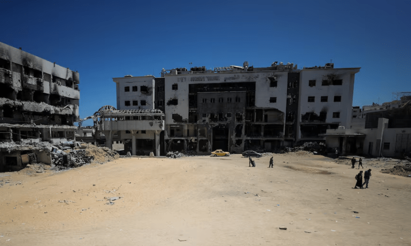  Palestinians walk next to a damaged building at Al-Shifa hospital, which is at risk of shutting down due to the Israeli blockade of fuel, in Gaza City on July 9, 2025. — Reuters/Mahmoud Issa 