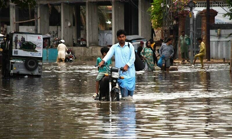 A man walks his motorcyle during the rain in Hyderabad’s Latifabad area on July 14. — Umair Ali
