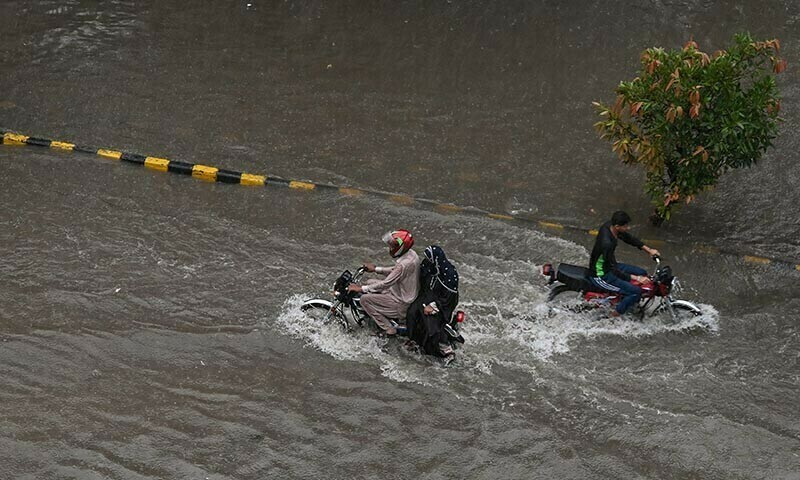 Commuters wade through a flooded street following heavy monsoon rains in Lahore on July 10, 2025. — AFP
