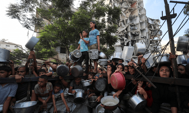 Palestinians wait to receive food from a charity kitchen, amid a hunger crisis, as a destroyed building stands in the background, in Gaza City on July 14, 2025. — Reuters