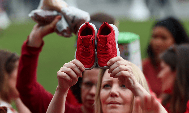 A woman holds a pair of little red shoes as people gather in Parliament Square wearing red and holding items behind a giant &lsquo;Red Line for Gaza&rsquo; banner to symbolise what is being lost due to the conflict, in London, Britain, on July 22. &mdash; Reuters