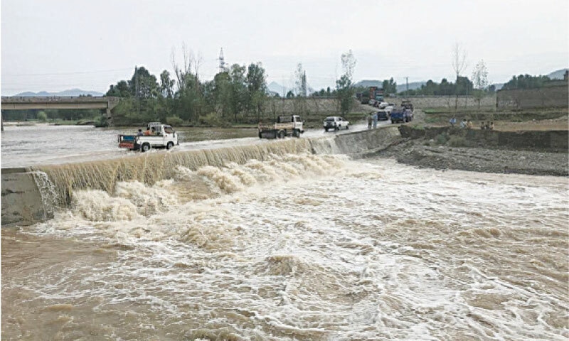 BAJAUR: Vehicles are stranded in the Jar area as rainwater accumulates on a temporary crossing, installed after a bridge was damaged.—Photo by Anwarullah