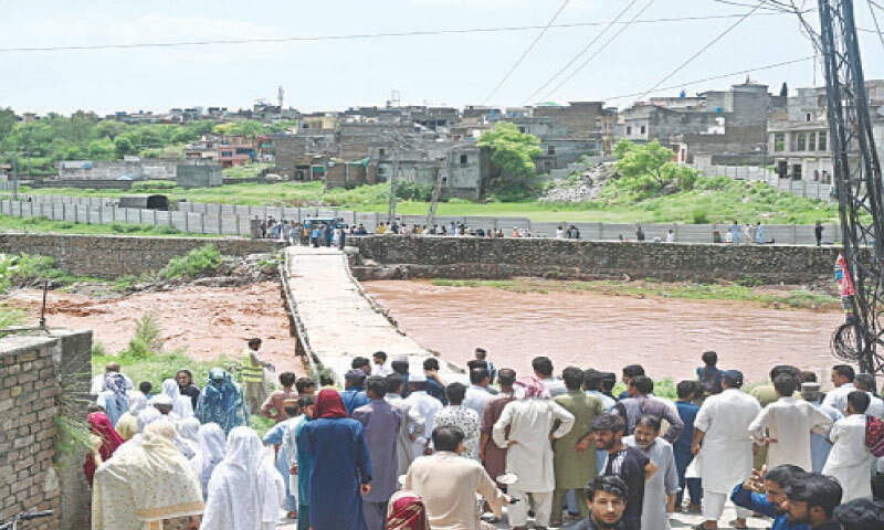 People gather along Korang Nullah at Sharifabad in Islamabad after water rose following the recent rains. Security personnel have stopped people from crossing the bridge after a man drowned in the nullah. — APP