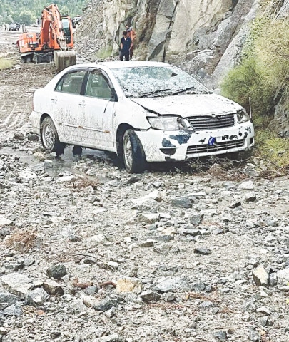  A DAMAGED car is parked on the road after being hit by a landslide as an excavator clears debris in Bargo Pari, Gilgit.—Dawn 