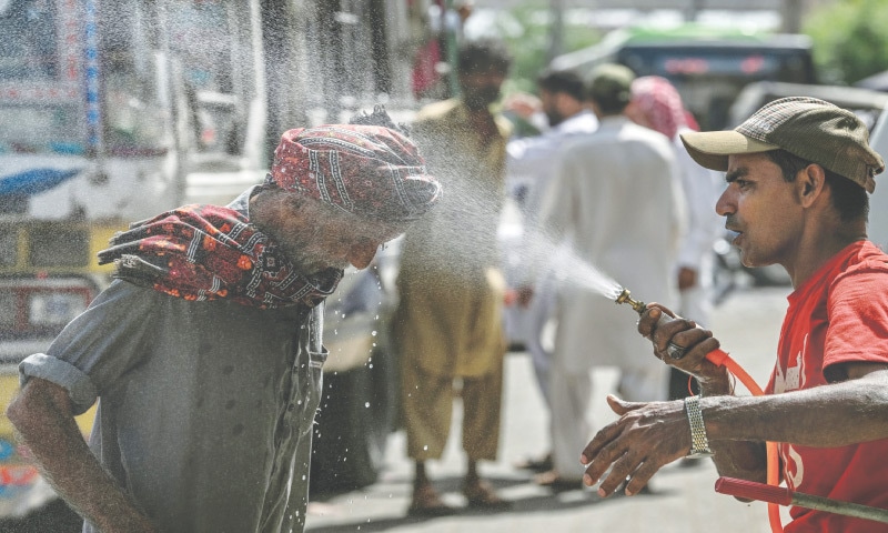 An Edhi Foundation volunteer sprays water on a passerby’s head on a hot summer day in Karachi on April 21, 2025: an unchecked increase in heat-retaining built-environments and the growing usage of air conditioners are further adding to heat stress felt inside microclimates | AFP