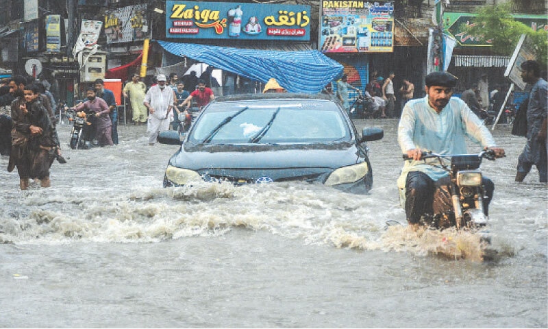 HYDERABAD: Commuters wade through a flooded street after heavy rains left many parts of Sindh inundated.—AFP