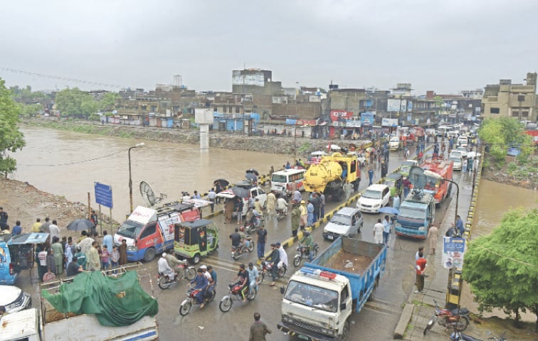  Vehicles cross a bridge in Gawalmandi as water surges to a dangerous level at Nullah Leh in Rawalpindi following intense rainfall on Thursday. — Photos by Mohammad Asim 