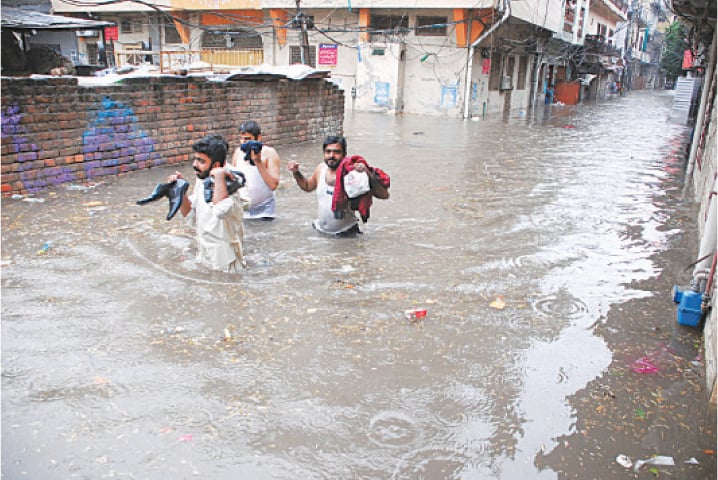  A group of men trying to keep their belongings dry while wading through waist-deep water, accumulated in a street in Rawalpindi’s Javed Colony area. — Photos by Mohammad Asim 