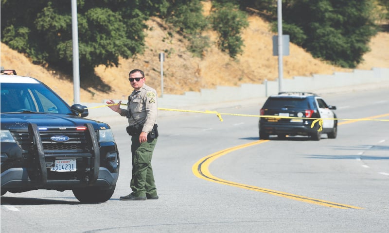 A COUNTY official lifts up yellow tape as he blocks the road to the training facility in Los Angeles where three ellow officers were killed following an explosion.—Reuters