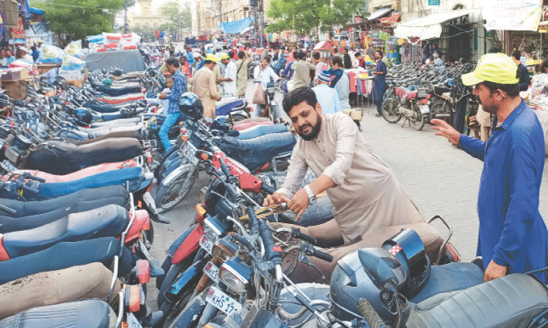 A man parks his motorbike on a Saddar road under the watchful eye of a parking attendant. The large number of parked motorbikes, which encroach upon more than half of the road, hints at the magnitude of the amount collected in the name of charged parking, with little oversight on a daily basis, in the metropolis.&mdash;Shakil Adil / White Star