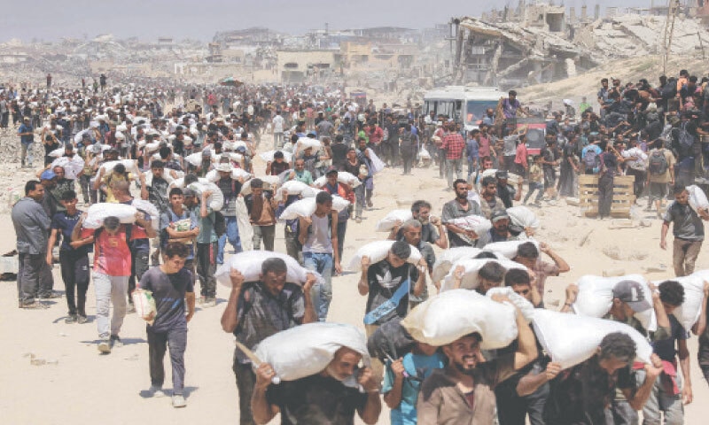 PALESTINIANS carry sacks of flour, delivered after trucks carrying humanitarian aid were finally allowed to enter northern Gaza through the Zikim border crossing.—AFP