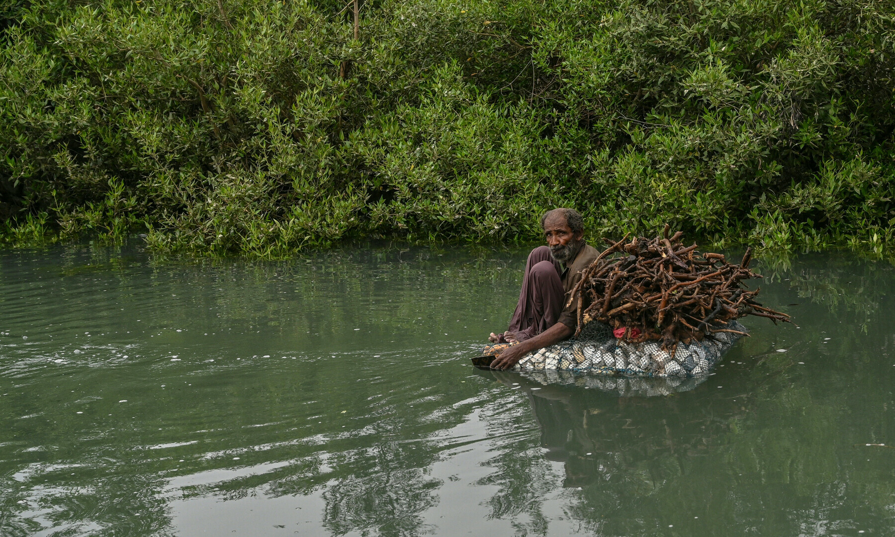 In this photograph taken on June 27, 2025, a fisherman rides a makeshift raft as he returns after collecting mangrove wood near the Arabian Sea on the coastal region of Karachi. &mdash; AFP