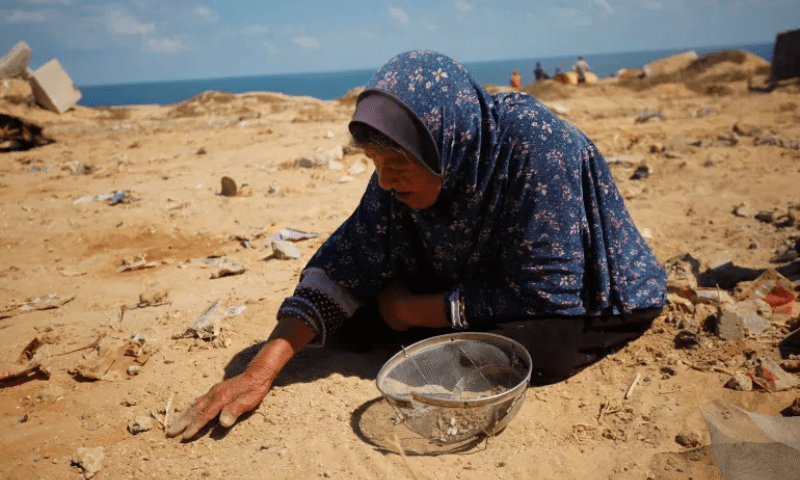 A Palestinian woman tries to pick rice, lentils, and beans out of sand, from aid packages that were dropped from the air and scattered upon impact in Gaza City. — Anadolu Agency