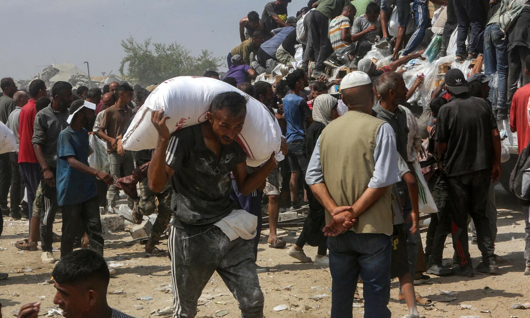 A man carries a bag of food as displaced Palestinians raid trucks carrying humanitarian aid in Khan Yunis, in the southern Gaza Strip on August 9, 2025. Nearly two years into the war in Gaza, Israel’s Prime Minister Benjamin Netanyahu faces mounting pressure to secure a truce to pull the territory’s more than two million people back from the brink of famine and free the hostages held by Palestinian militants. (Photo by AFP)