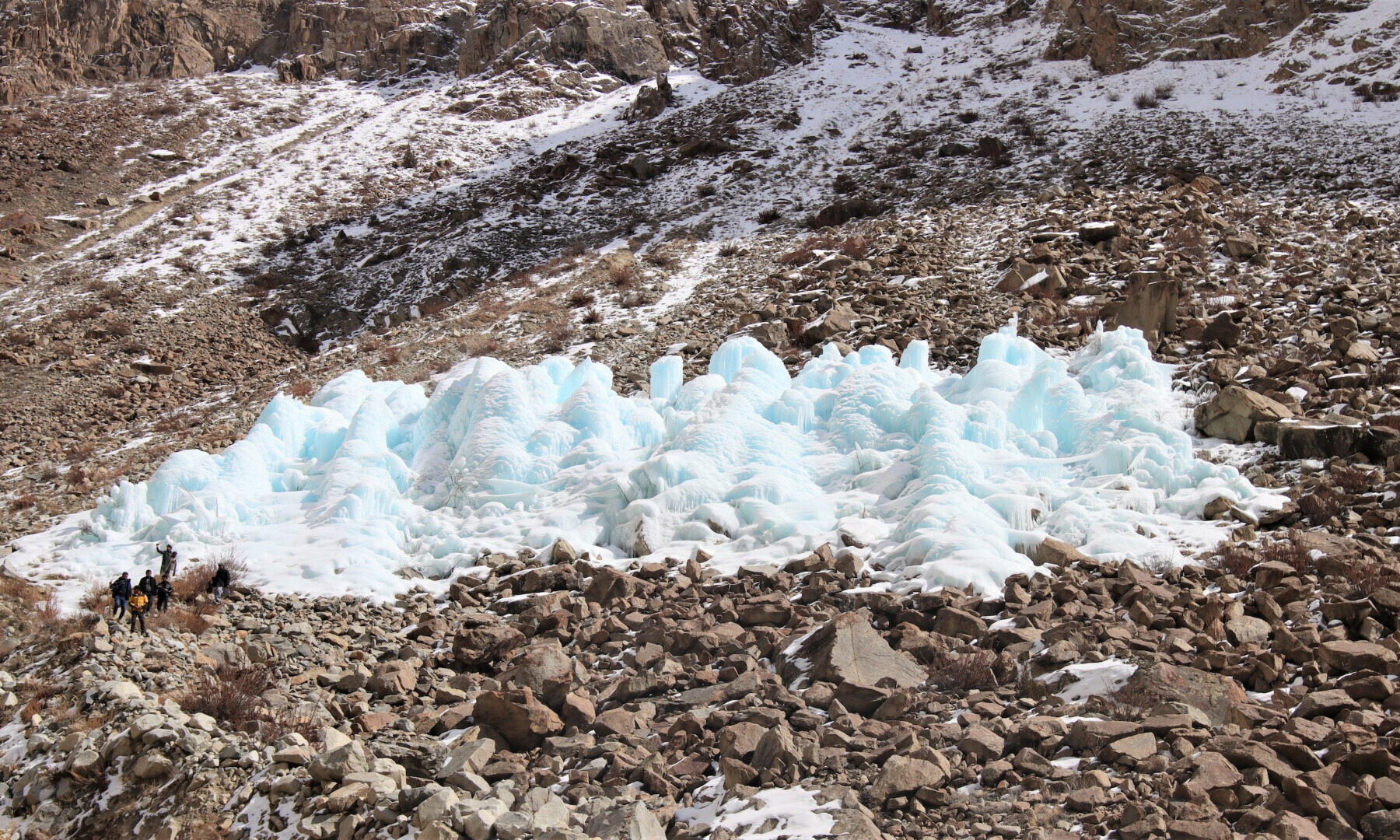 Ice stupas such as this one in Gilgit-Baltistan, are massive artificial glaciers, shown here with people standing at its foot (bottom left). In the region, they are created on the side of mountains using water piped from streams at higher elevation (Image: UNDP)