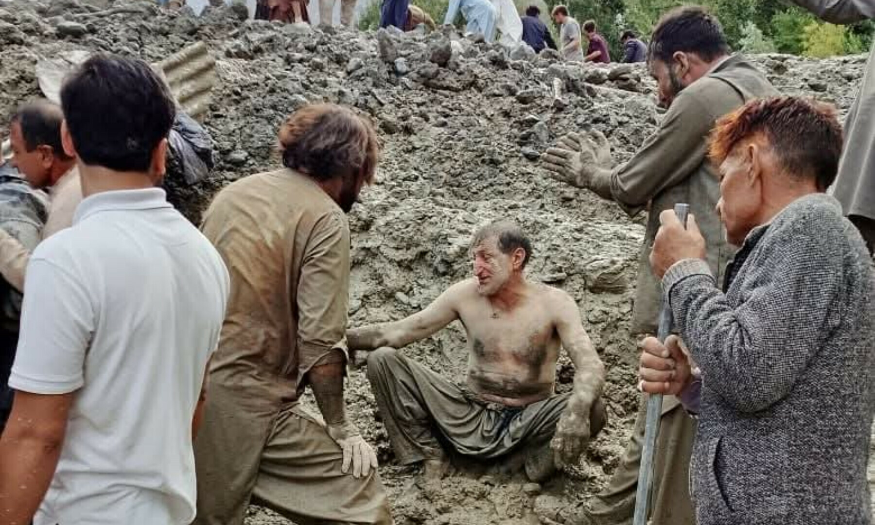  A flood-affected person sits as people gather around following flash floods in GB’s Ghizer on Aug 15, 2025. — Jamil Nagri 