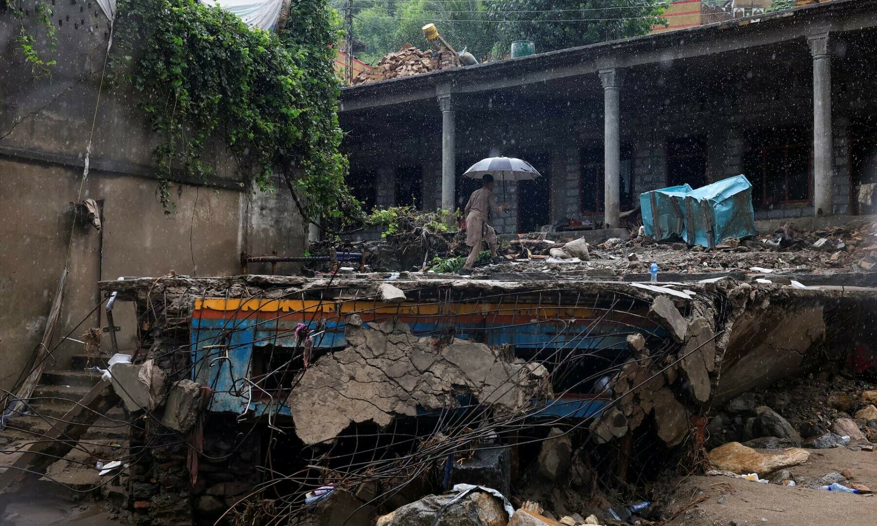 A resident walks with an umbrella to avoid rain at the damaged house, following a storm that caused heavy rains and flooding in Bayshonai Kalay, in Buner district, in Khyber Pakhtunkhwa province. — Reuters