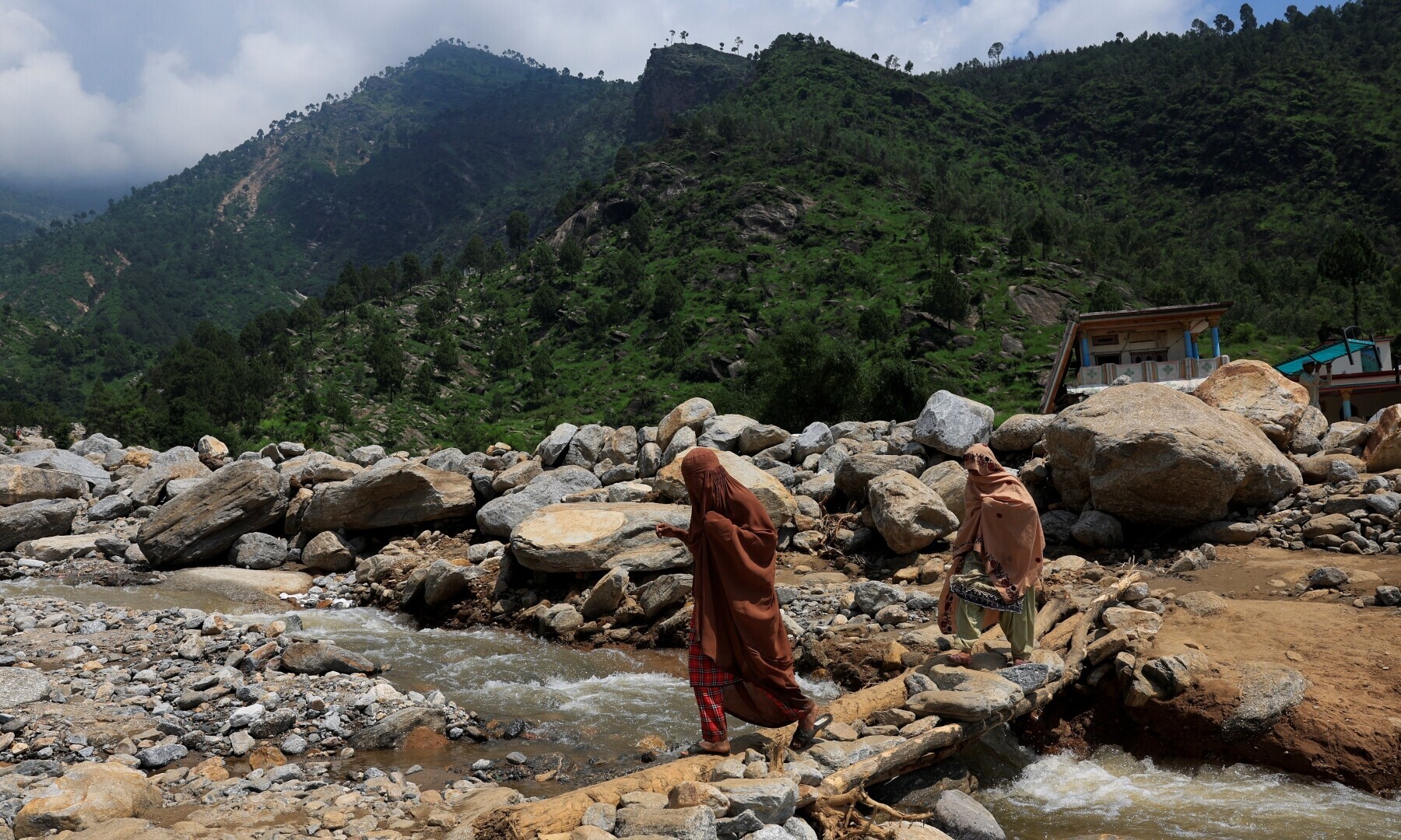 Women walk on a makeshift bridge made of rocks and wood, following a storm that causes heavy rains and flooding in the Qadir Nagar area, KP&rsquo;s Buner district on August 21. &mdash; Reuters