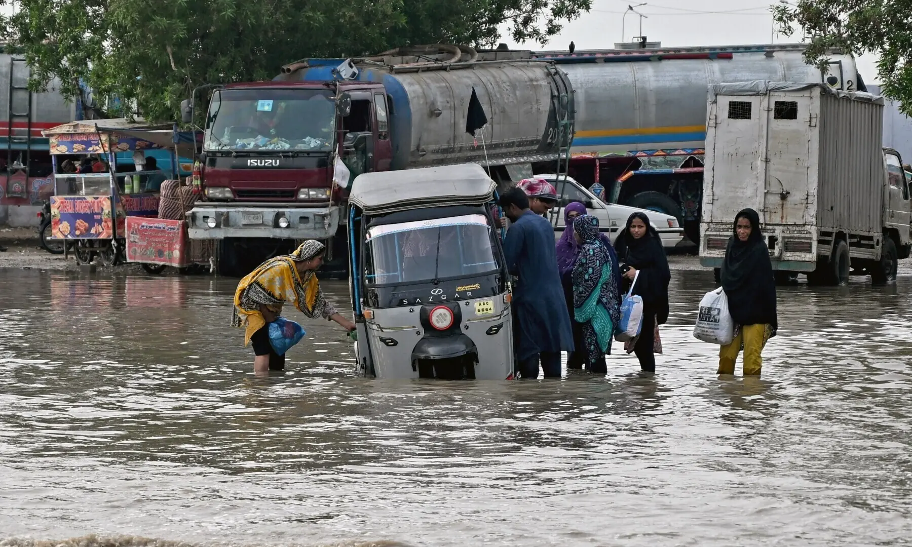 Passengers disembark from an auto rickshaw that got stranded on a flooded road after heavy monsoon rains in Karachi on August 20, 2025. &mdash; AFP