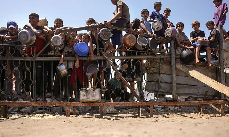 Children gather by a fence as they try to get rice from a charity kitchen providing food for free in the west of Gaza City on August 28. — AFP