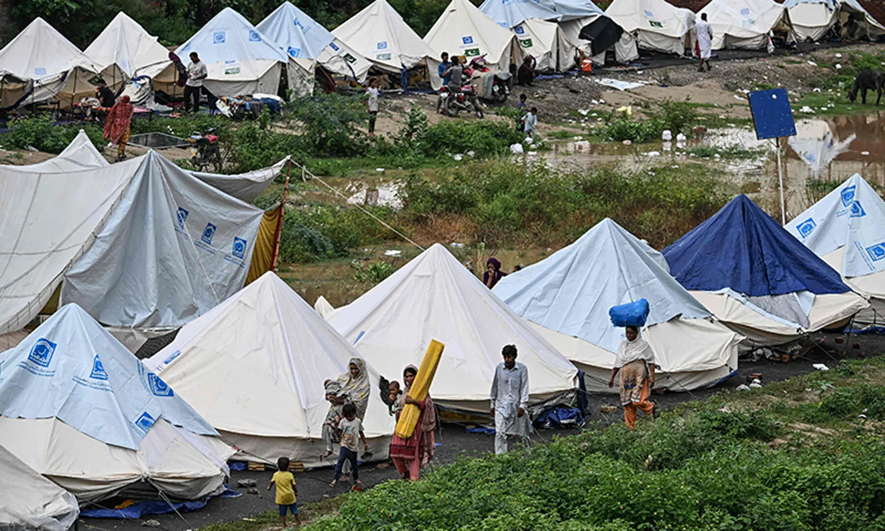 Flood victims walk along shelters at a makeshift camp in Chung, near Lahore on August 31. — AFP