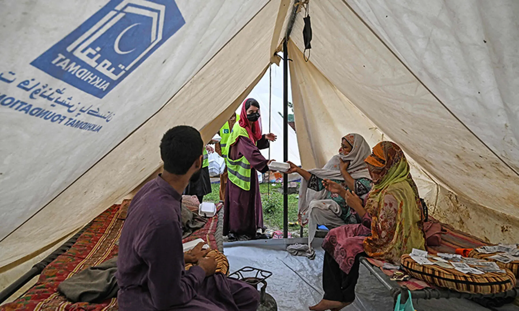A volunteer (C) distributes food to flood victims at a makeshift camp in Chung, near Lahore on August 31. — AFP